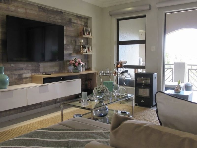 A well-maintained living room featuring a modern built-in media console, decorative wood-look feature wall, and direct access to a private balcony.