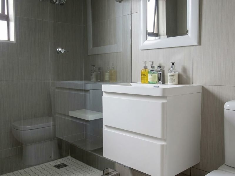 Modern bathroom featuring a wall-mounted vanity, glass-enclosed shower, and neutral tiled finishes, providing a clean and contemporary aesthetic.