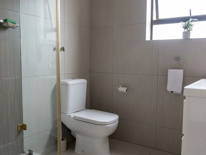 A modern bathroom featuring a glass-enclosed shower, a white vanity with basin, and neutral wall tiling, complemented by a top-hung window for natural light.