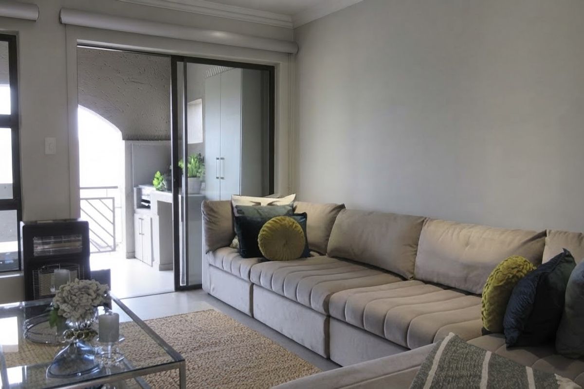 A bright living room featuring neutral walls, cove cornicing, and a large sliding glass door providing access to an outdoor balcony area.