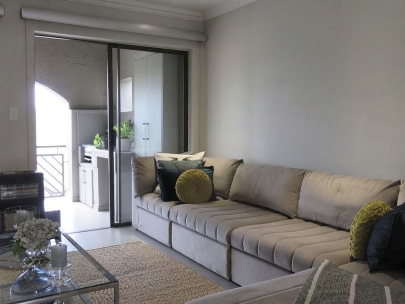 A bright living room featuring neutral walls, cove cornicing, and a large sliding glass door providing access to an outdoor balcony area.