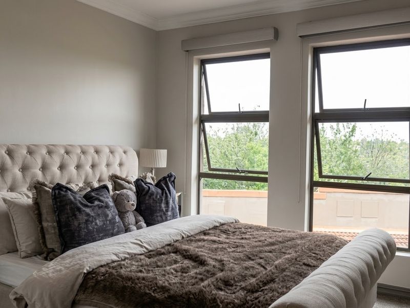 A well-maintained bedroom featuring neutral walls, modern aluminium window frames, and roller blinds, offering a comfortable and bright living space.