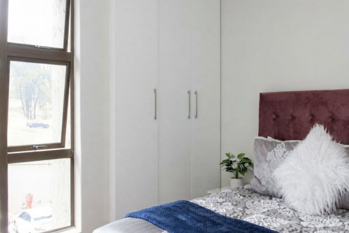 A well-maintained bedroom featuring built-in cupboards and a large aluminium window providing natural light.