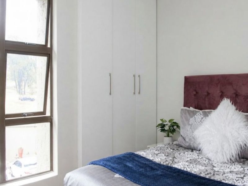 A well-maintained bedroom featuring built-in cupboards and a large aluminium window providing natural light.