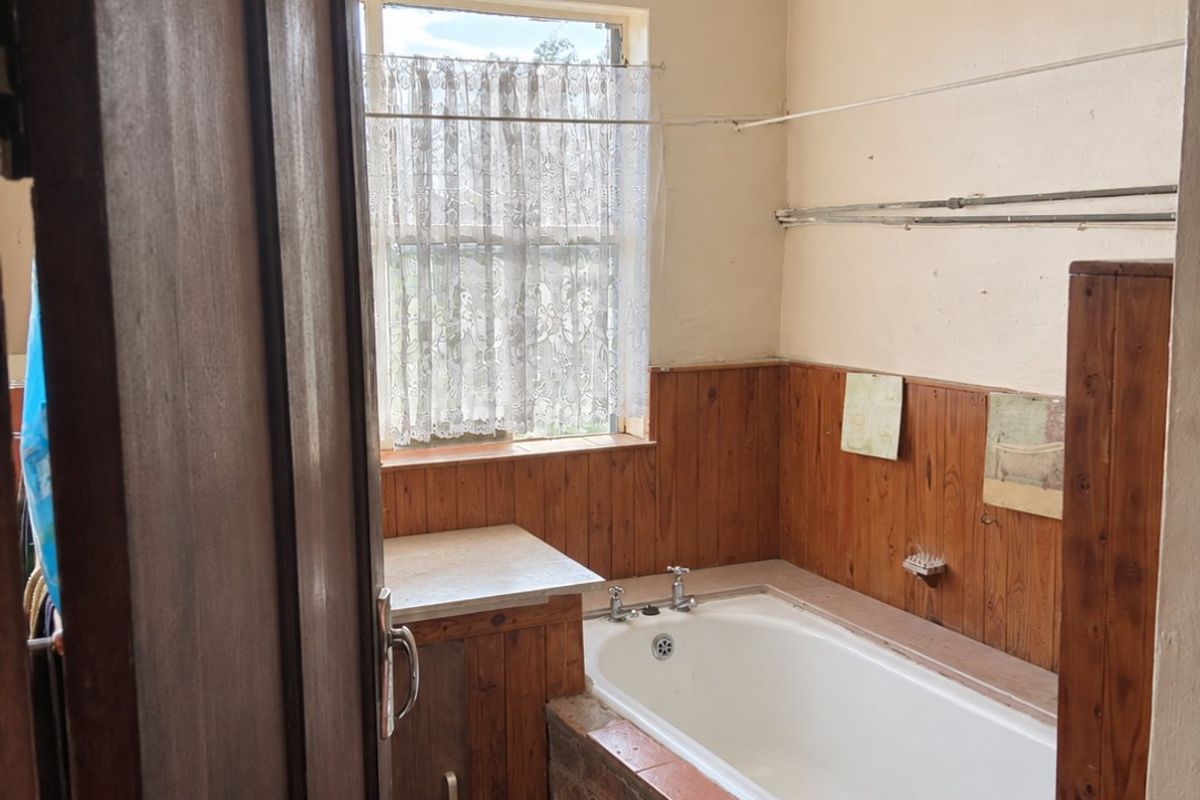 A dated bathroom featuring a built-in bathtub with an exposed brick surround, timber wall paneling, and a timber vanity unit.