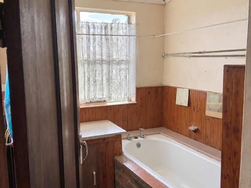 A dated bathroom featuring a built-in bathtub with an exposed brick surround, timber wall paneling, and a timber vanity unit.