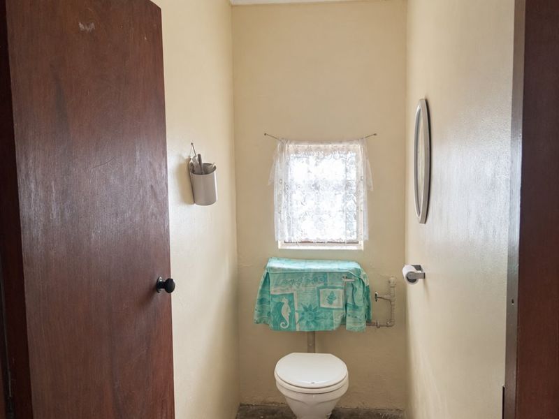 A compact, functional bathroom featuring a standard toilet and window, currently requiring cosmetic updates to the flooring and wall finishes.