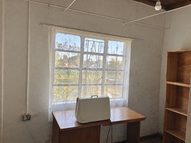 A bedroom space featuring exposed timber ceiling beams, a window with security bars, and wall surfaces in need of cosmetic repair and repainting.