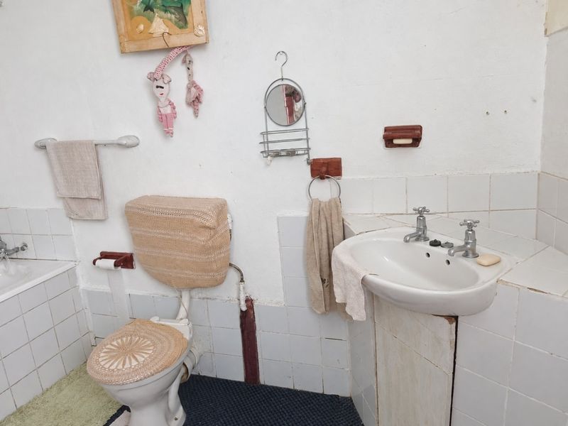 A dated bathroom featuring a pedestal basin, toilet, and bathtub with tiled splashbacks, requiring modernization of fixtures and finishes.