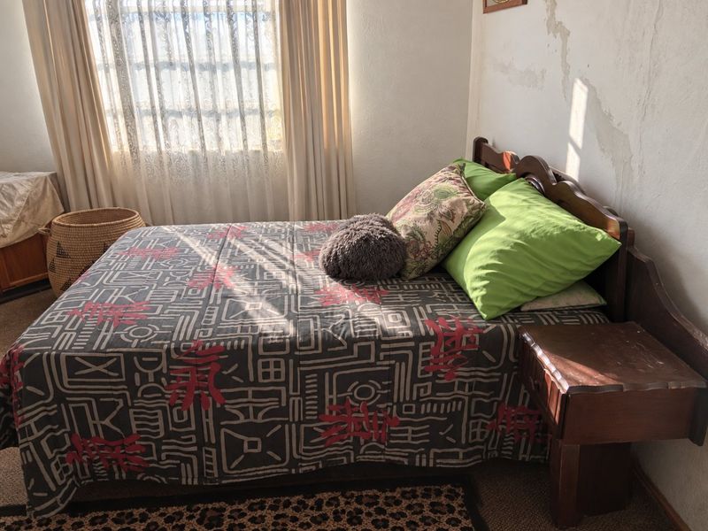 A bedroom featuring natural light from a window with curtains, showing visible signs of wall water damage and paint deterioration.