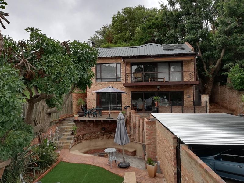 Rear view of a two-story brick house featuring a timber balcony, sunken fire pit area, paved patio, and a covered carport.