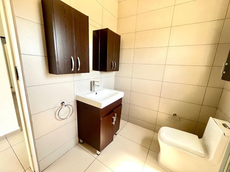 A clean, modern bathroom featuring a vanity unit with storage, wall-mounted cabinets, a ceramic basin, and a toilet, finished with neutral wall and floor tiles.