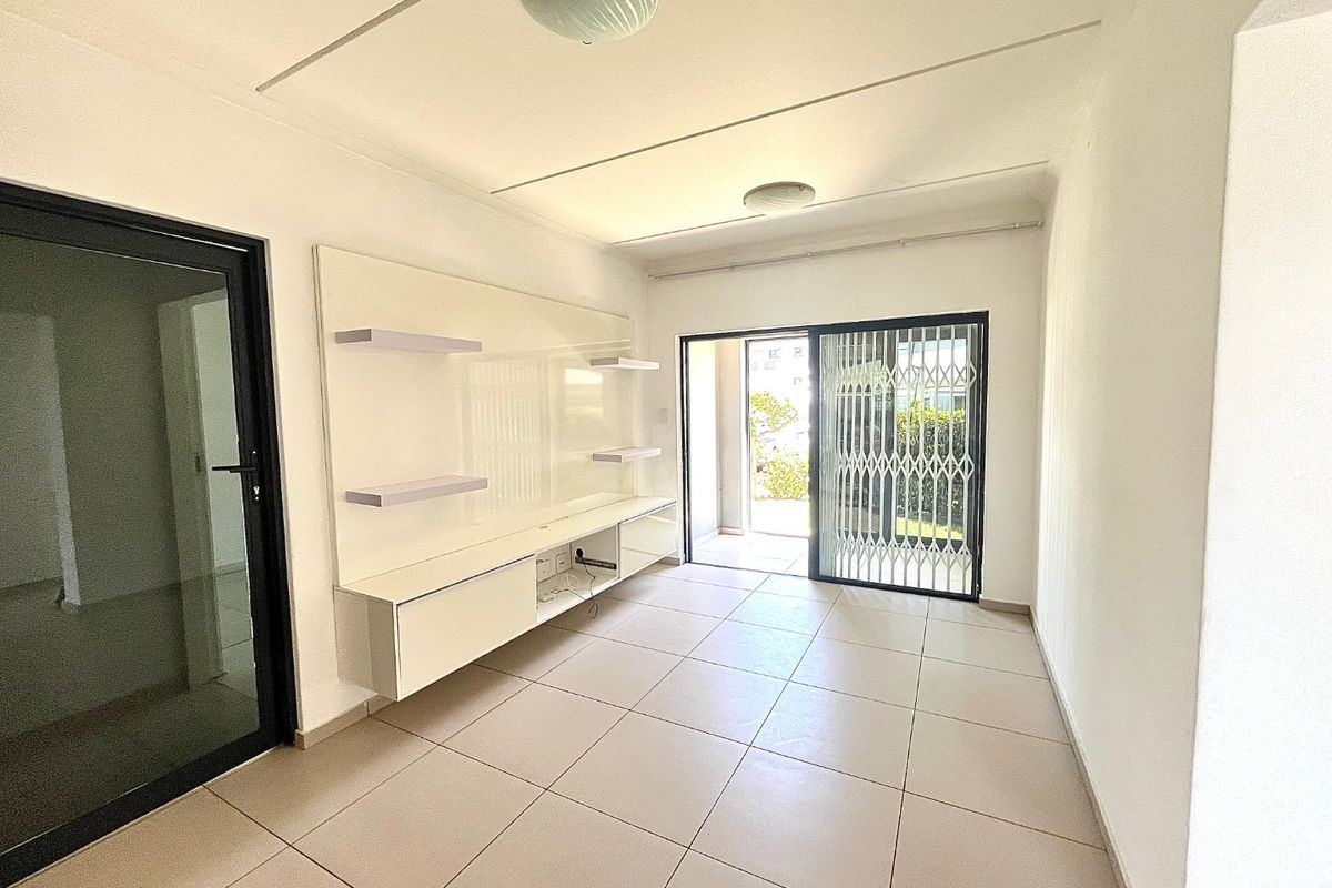 A bright, empty living room featuring neutral tiled flooring, a built-in media console, and a sliding glass door leading to an outdoor area.