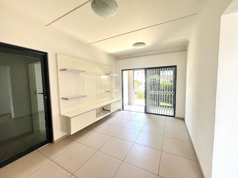 A bright, empty living room featuring neutral tiled flooring, a built-in media console, and a sliding glass door leading to an outdoor area.