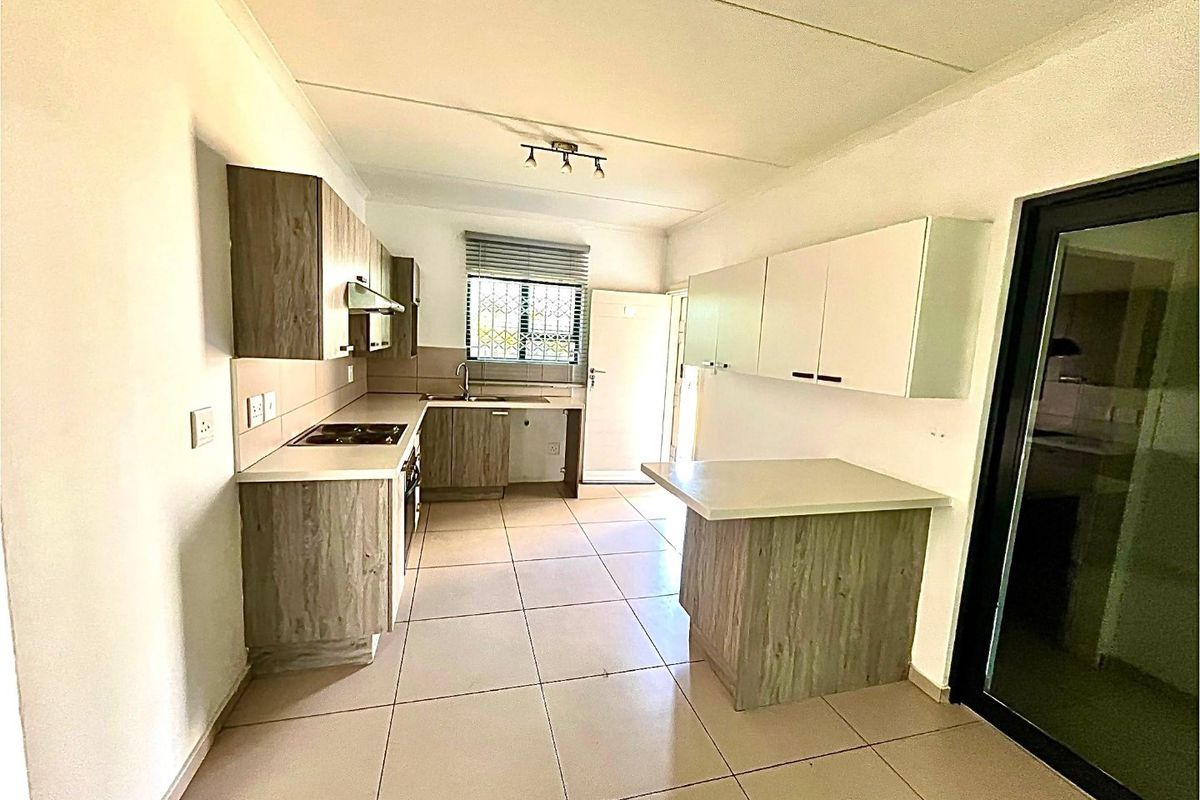 A clean, functional kitchen featuring modern wood-look cabinetry, tiled flooring, built-in oven and hob, and a breakfast counter, offering a bright and practical workspace.