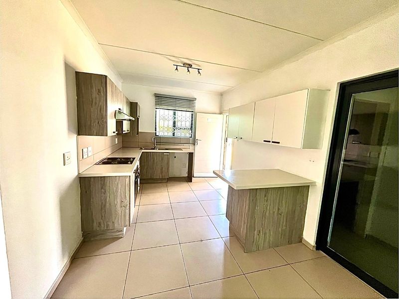 A clean, functional kitchen featuring modern wood-look cabinetry, tiled flooring, built-in oven and hob, and a breakfast counter, offering a bright and practical workspace.