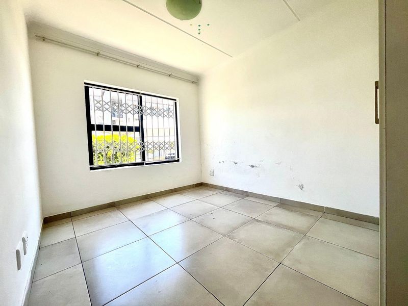 An empty bedroom featuring tiled flooring and a window with a security gate. The walls show signs of wear and require maintenance.