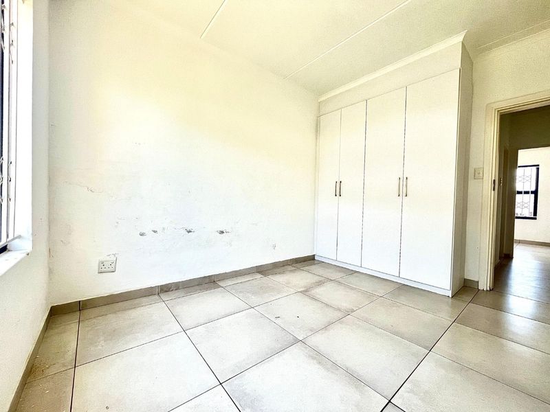 An empty bedroom featuring tiled flooring and built-in cupboards, requiring minor cosmetic repairs to the wall surfaces.