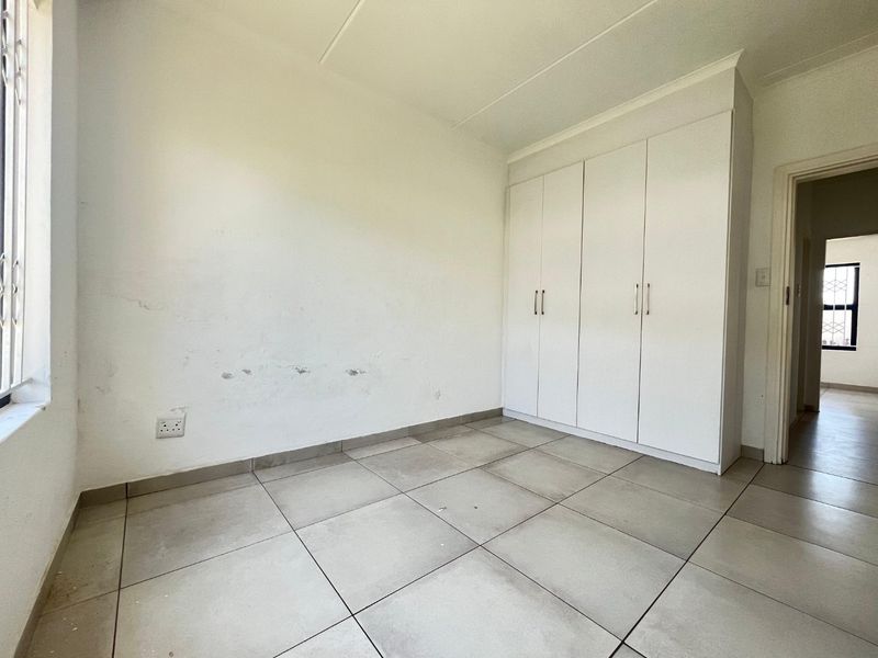 An empty bedroom featuring tiled flooring and built-in cupboards, requiring minor cosmetic attention to the walls.