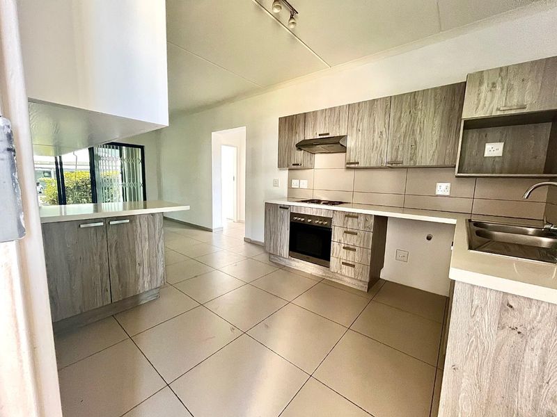 A clean, modern kitchen featuring wood-look cabinetry, built-in oven and hob, tiled flooring, and a functional layout with ample counter space.