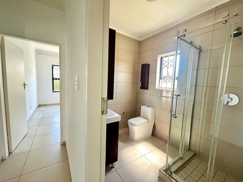 A clean, modern bathroom featuring a glass shower enclosure, wall-mounted vanity, and neutral ceramic tiling throughout.