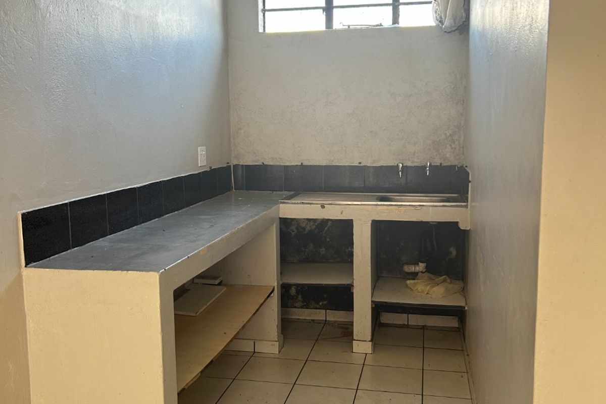 A basic, functional kitchen area featuring concrete countertops, a stainless steel sink, and tiled flooring, currently in need of renovation and cosmetic updates.