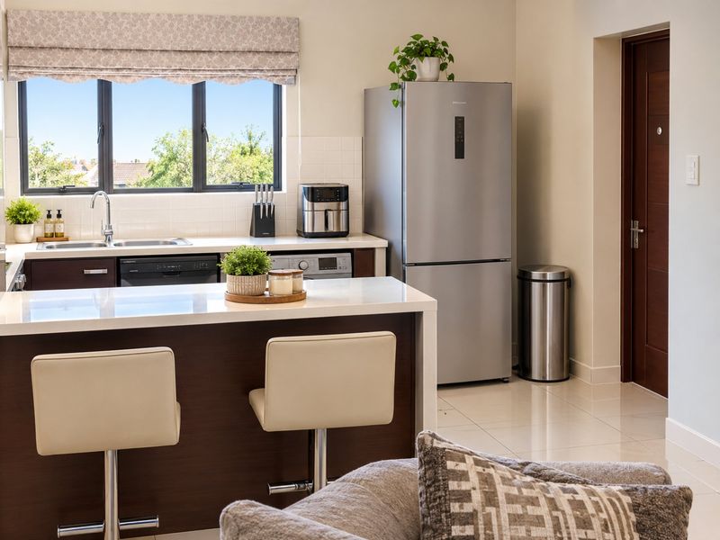 Modern kitchen featuring dark wood cabinetry, white quartz countertops, tiled backsplash, and integrated appliances, with a breakfast bar and large window.