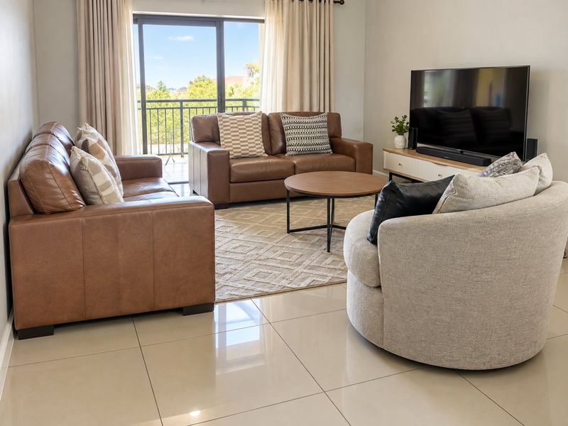 A bright and spacious living room featuring large format tile flooring and a sliding glass door providing direct access to a private balcony.