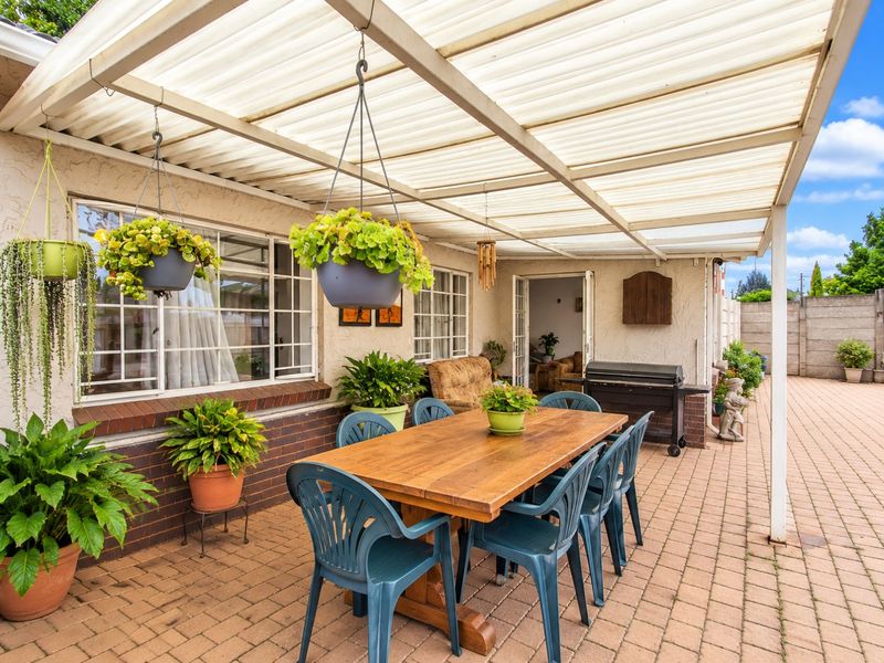 A covered outdoor patio area featuring brick paving, a corrugated roof structure, and direct access to the home through sliding glass doors.