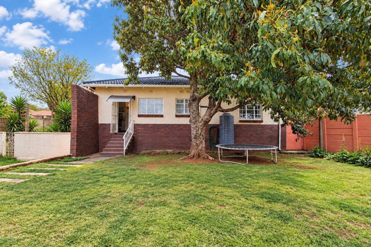 Rear view of the house featuring a brick and plaster facade, mature tree, and a spacious lawn area.