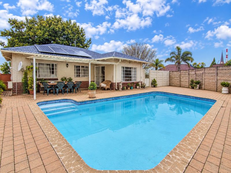 Outdoor pool area featuring a paved patio, covered veranda, and solar panels installed on the tiled roof, enclosed by a brick boundary wall.