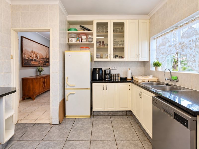 A functional kitchen featuring granite countertops, double basin sink, and ample built-in cabinetry with tiled flooring and wall finishes.