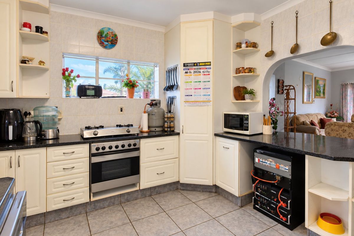 A functional kitchen featuring built-in cabinetry, granite countertops, a gas stove with oven, and tiled finishes, with an open-plan flow to the living area.