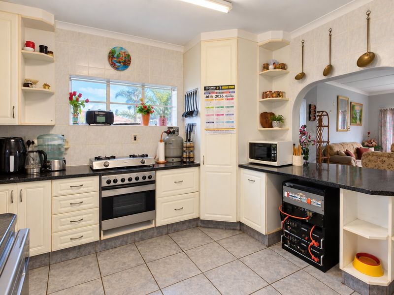 A functional kitchen featuring built-in cabinetry, granite countertops, a gas stove with oven, and tiled finishes, with an open-plan flow to the living area.