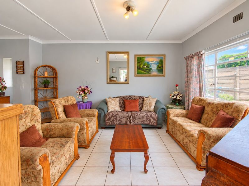 A well-lit living room featuring neutral tiled flooring, coved ceilings, and a large window providing natural light.