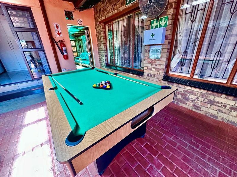 A covered patio area featuring exposed brick walls, tiled flooring, and security-fitted glass doors, currently utilized as a recreational space.