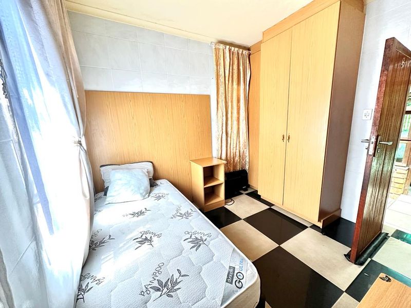A compact bedroom featuring built-in wooden cabinetry, tiled flooring, and wall cladding, offering a functional space with potential for modern updates.