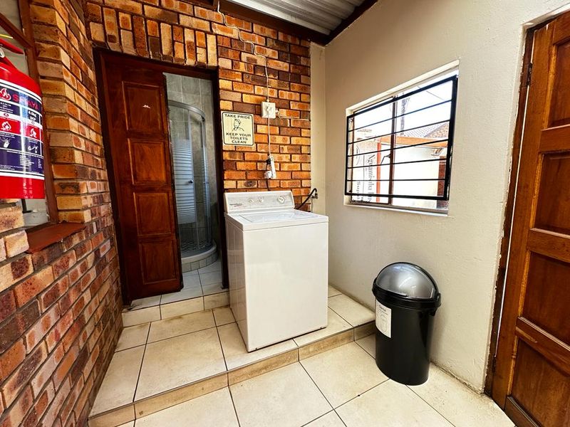 A functional laundry area featuring exposed brick walls, tiled flooring, and direct access to an adjacent bathroom facility.
