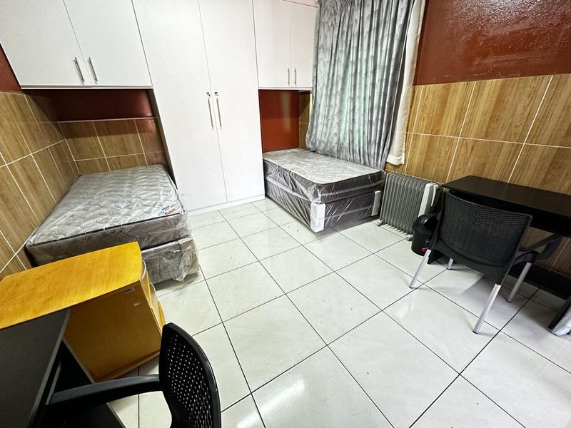 A bedroom featuring built-in cupboards, tiled flooring, and tiled wall accents, providing a functional space with integrated storage solutions.