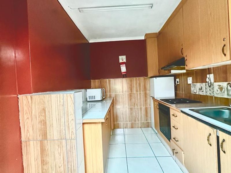 A functional kitchen featuring laminate cabinetry, built-in oven, electric hob, extractor fan, and tiled backsplash with neutral floor tiles.
