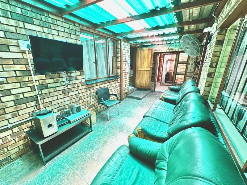 A covered outdoor patio area featuring exposed brick walls, tiled flooring, and a translucent roof, currently utilized as an informal entertainment space.