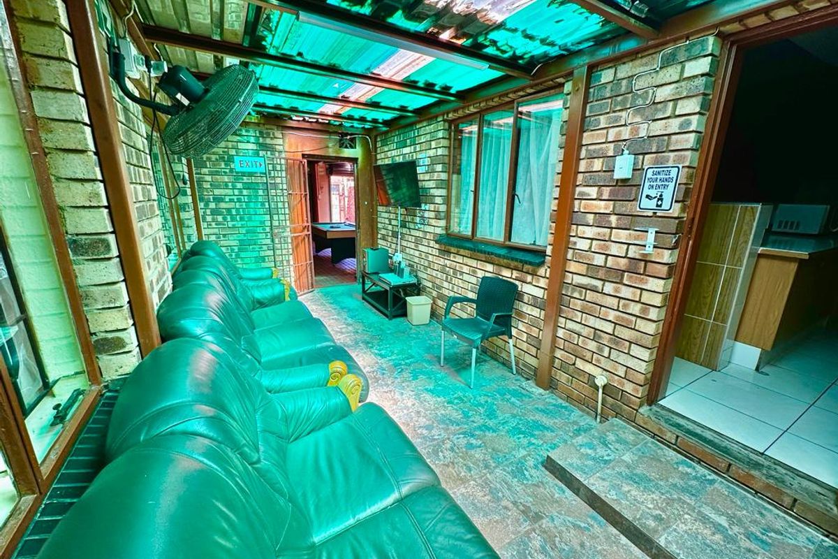 A covered outdoor patio area featuring exposed brick walls, tiled flooring, and a translucent roof, providing a functional space for relaxation.