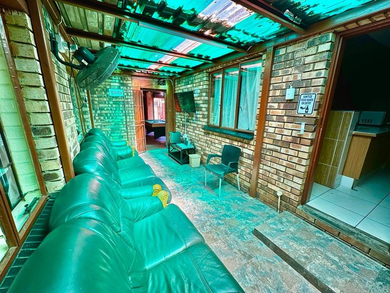 A covered outdoor patio area featuring exposed brick walls, tiled flooring, and a translucent roof, providing a functional space for relaxation.