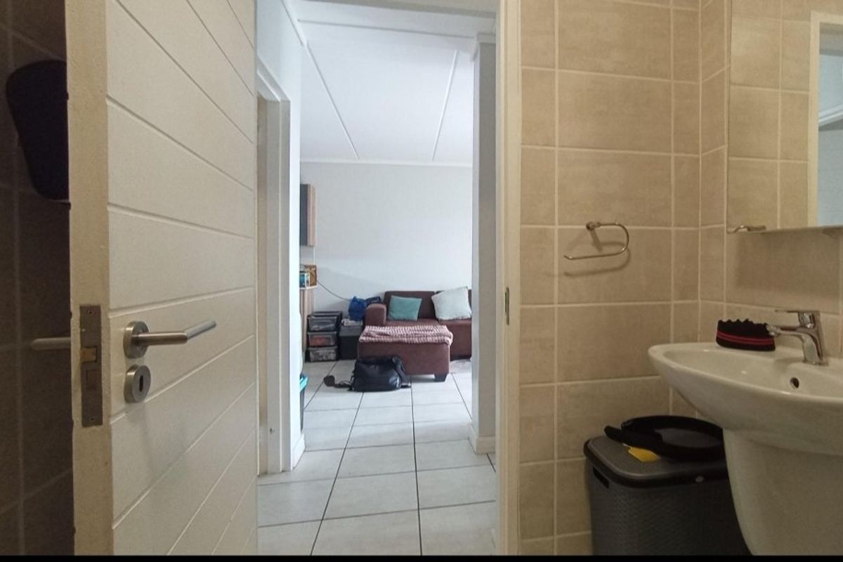 A view from a tiled bathroom looking through a doorway into an adjacent living area with matching floor tiles.
