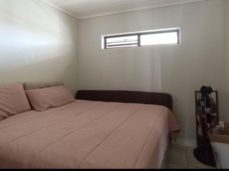A compact bedroom featuring neutral wall finishes, tiled flooring, and a high-set horizontal window providing natural light.