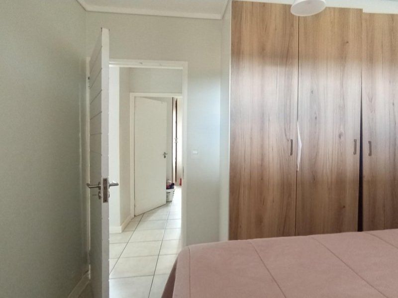 A bedroom featuring built-in wooden cupboards and tiled flooring, with an open doorway leading to a hallway.