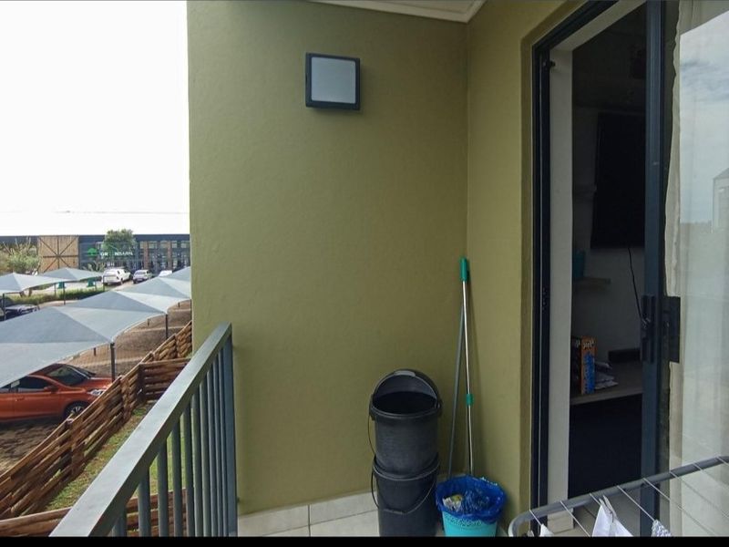 A functional apartment balcony featuring tiled flooring, a metal balustrade, and a sliding glass door providing access to the interior living space.