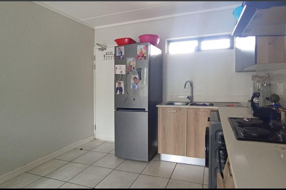 A functional kitchen featuring built-in cabinetry, a double sink, and a hob with an extractor fan, finished with tiled flooring.