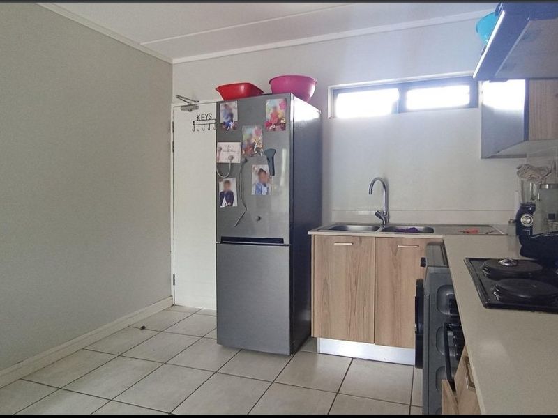 A functional kitchen featuring built-in cabinetry, a double sink, and a hob with an extractor fan, finished with tiled flooring.