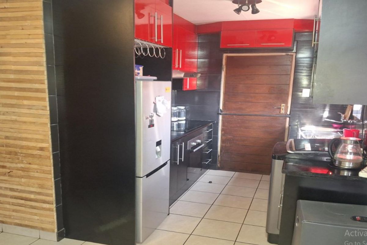 A compact kitchen featuring high-gloss red and black cabinetry, tiled flooring, and a wooden door leading to the exterior.